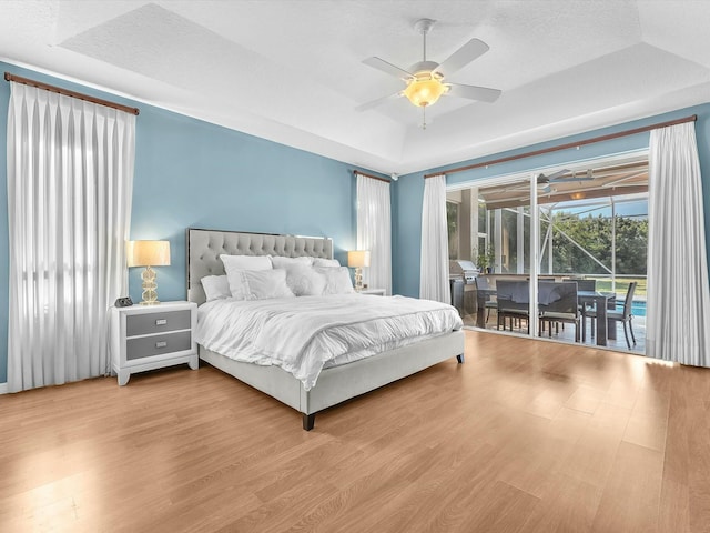 bedroom featuring a tray ceiling, access to outside, a textured ceiling, and light wood-type flooring