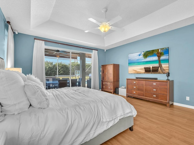 bedroom with a raised ceiling, access to exterior, a textured ceiling, and light hardwood / wood-style flooring