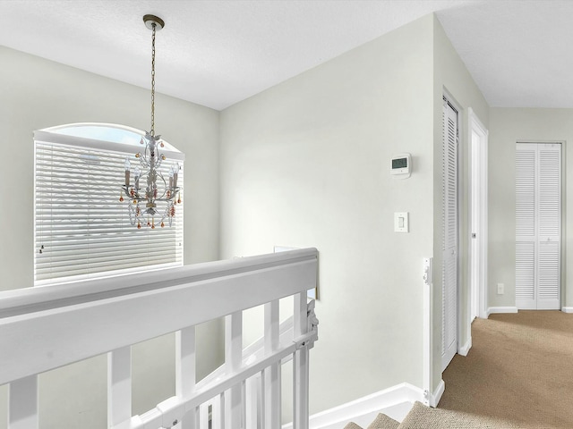 corridor with an inviting chandelier and carpet flooring