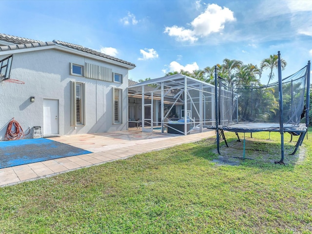 back of property with a trampoline, a yard, and a patio area