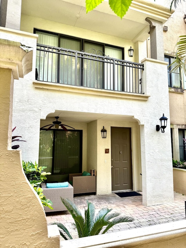 entrance to property featuring a balcony, ceiling fan, and stucco siding