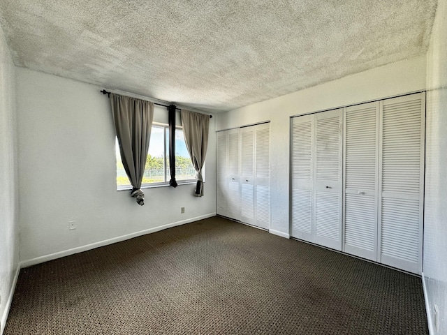 unfurnished bedroom with multiple closets, a textured ceiling, and dark colored carpet