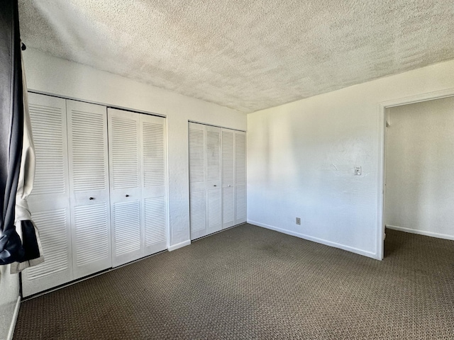 unfurnished bedroom with multiple closets, a textured ceiling, and dark colored carpet