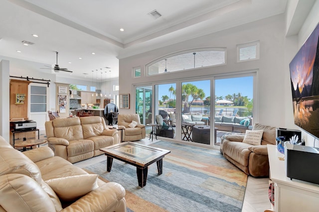 living room featuring ceiling fan, a high ceiling, a tray ceiling, a barn door, and light parquet flooring