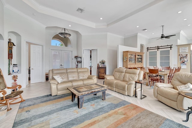 living room with a towering ceiling, a tray ceiling, ornamental molding, a barn door, and light parquet flooring