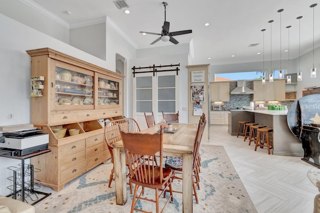 dining space featuring ceiling fan, ornamental molding, a barn door, and light parquet flooring