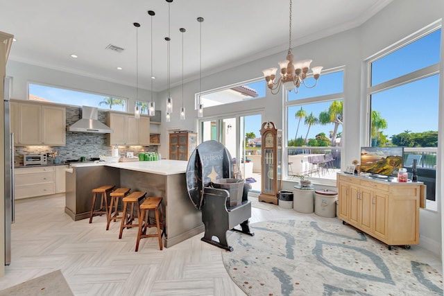 kitchen featuring wall chimney range hood, crown molding, a spacious island, tasteful backsplash, and light brown cabinets