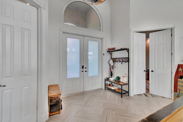 foyer entrance featuring a towering ceiling, french doors, and light parquet floors