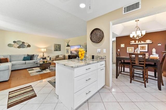 kitchen with decorative light fixtures, white cabinetry, a chandelier, light tile patterned floors, and light stone counters