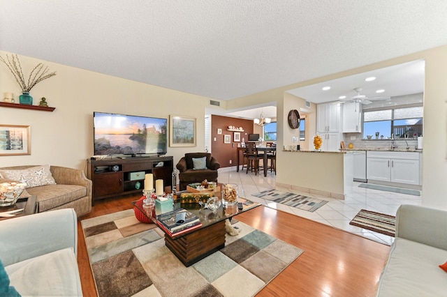 living room featuring light tile patterned floors, ceiling fan with notable chandelier, sink, and a textured ceiling