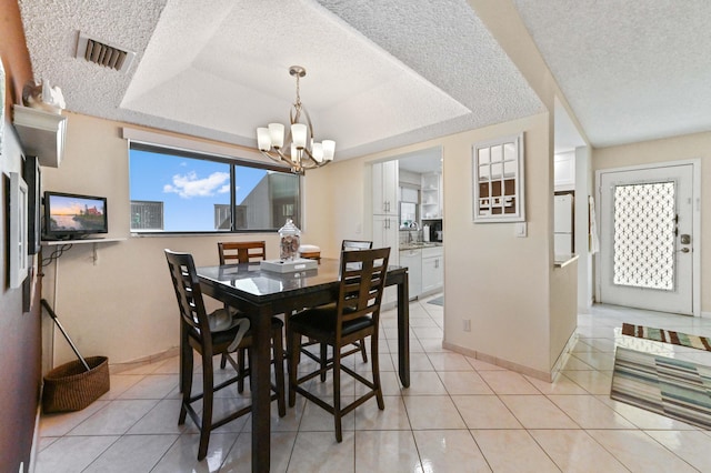 dining space with an inviting chandelier, light tile patterned floors, a textured ceiling, and a tray ceiling