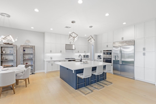 kitchen with a breakfast bar area, decorative light fixtures, an island with sink, stainless steel appliances, and white cabinets