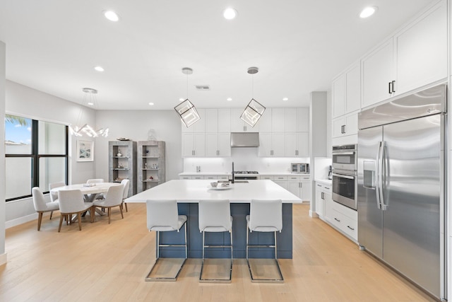 kitchen featuring appliances with stainless steel finishes, decorative light fixtures, an island with sink, a breakfast bar area, and white cabinets