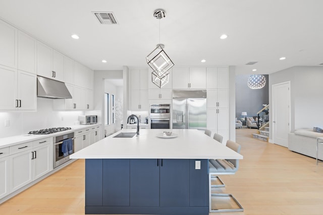 kitchen with stainless steel appliances, sink, decorative light fixtures, and a kitchen island with sink