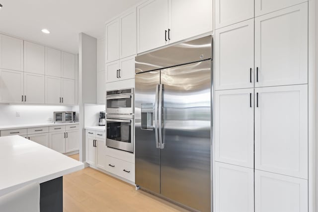 kitchen with appliances with stainless steel finishes, white cabinets, and light hardwood / wood-style flooring