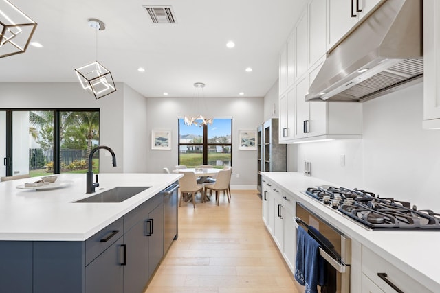 kitchen featuring appliances with stainless steel finishes, white cabinetry, sink, hanging light fixtures, and a kitchen island with sink