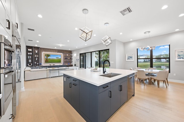 kitchen featuring light hardwood / wood-style floors, decorative light fixtures, a kitchen island with sink, and sink