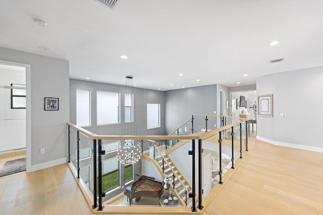 hall with plenty of natural light, light hardwood / wood-style floors, and a chandelier