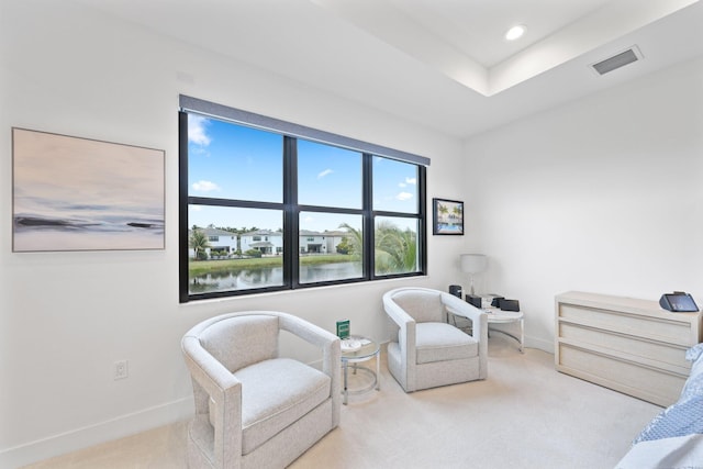 living area featuring light carpet, a tray ceiling, and a water view