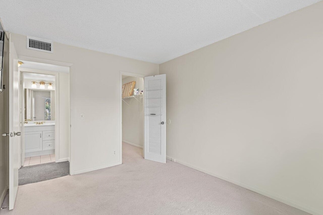 unfurnished bedroom with a walk in closet, light carpet, a textured ceiling, and a closet