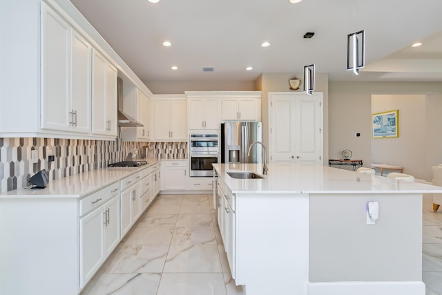 kitchen with appliances with stainless steel finishes, white cabinetry, sink, a kitchen island with sink, and wall chimney exhaust hood