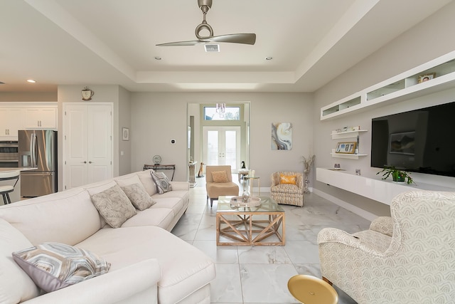 living room with a raised ceiling, ceiling fan, and french doors