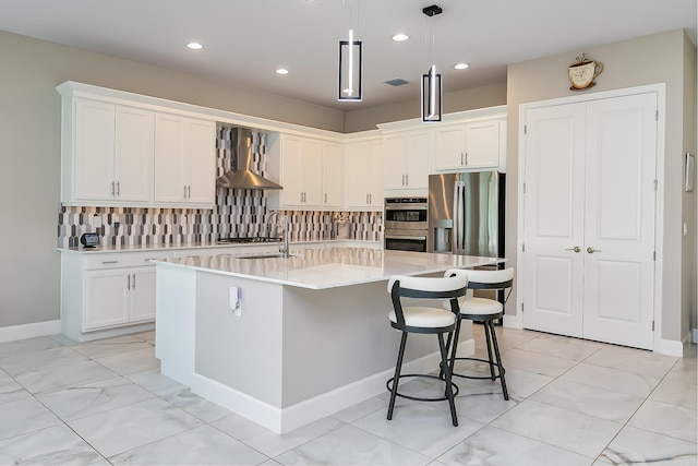 kitchen featuring appliances with stainless steel finishes, an island with sink, sink, white cabinets, and wall chimney range hood