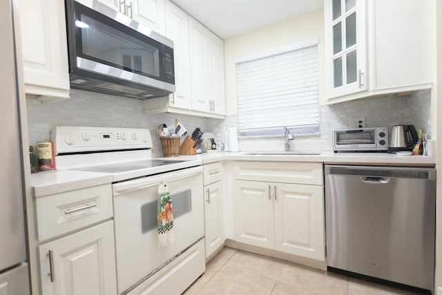 kitchen with sink, tasteful backsplash, light tile patterned floors, appliances with stainless steel finishes, and white cabinets