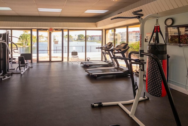 exercise room featuring a water view, a healthy amount of sunlight, and a paneled ceiling