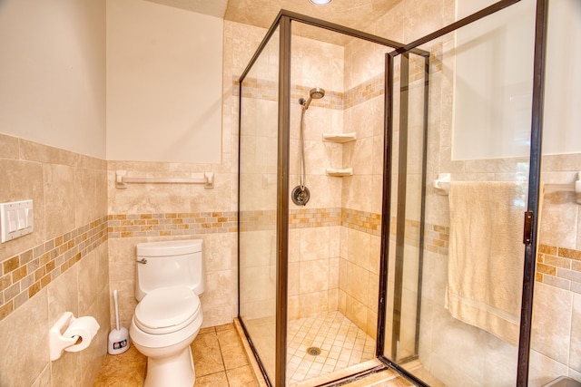 bathroom with tile walls, toilet, a stall shower, and tile patterned floors