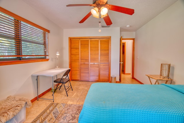 bedroom with a closet, light tile patterned floors, a textured ceiling, and baseboards