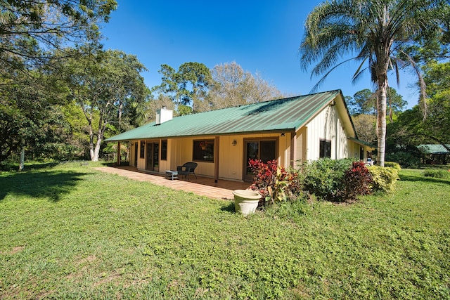 rear view of house featuring metal roof, a yard, a patio area, and a chimney