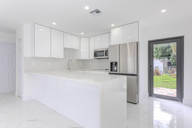 kitchen with sink, kitchen peninsula, white cabinets, stainless steel appliances, and backsplash