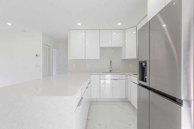 kitchen featuring sink, stainless steel fridge, white cabinetry, decorative backsplash, and kitchen peninsula