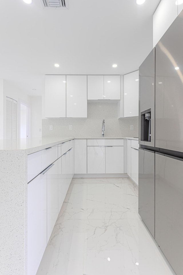 kitchen featuring stainless steel refrigerator with ice dispenser, backsplash, sink, and white cabinets