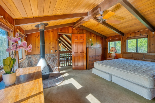 carpeted bedroom featuring lofted ceiling with beams, wooden walls, wood ceiling, and a wood stove