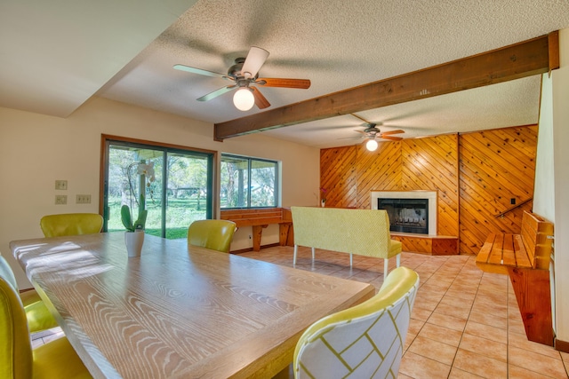 dining room with beam ceiling, a fireplace, wood walls, and a textured ceiling