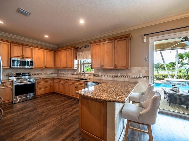 kitchen with sink, appliances with stainless steel finishes, dark stone countertops, a kitchen breakfast bar, and decorative backsplash