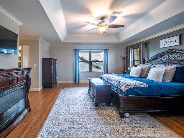 bedroom featuring hardwood / wood-style flooring, ornamental molding, ceiling fan, and a tray ceiling