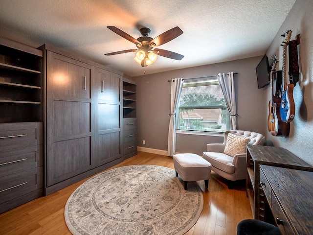 living area with ceiling fan, light hardwood / wood-style flooring, and a textured ceiling