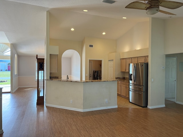 kitchen featuring light wood finished floors, stainless steel fridge, arched walkways, a ceiling fan, and light stone countertops