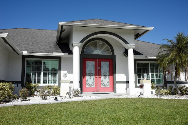 property entrance with a shingled roof, a lawn, and stucco siding