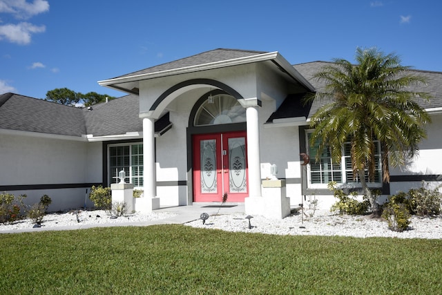 property entrance featuring a yard, a shingled roof, french doors, and stucco siding