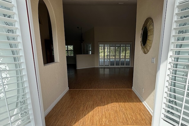 hall with baseboards, arched walkways, wood finished floors, and a textured wall