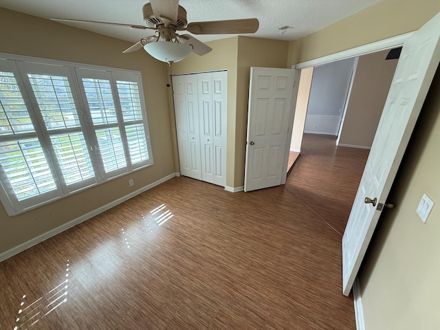 unfurnished bedroom featuring a closet, ceiling fan, a textured ceiling, wood finished floors, and baseboards