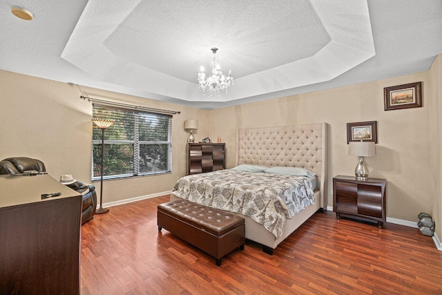 bedroom featuring dark hardwood / wood-style flooring, a tray ceiling, a chandelier, and a textured ceiling