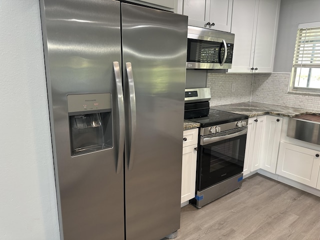 kitchen featuring appliances with stainless steel finishes, white cabinets, dark stone counters, decorative backsplash, and light hardwood / wood-style floors