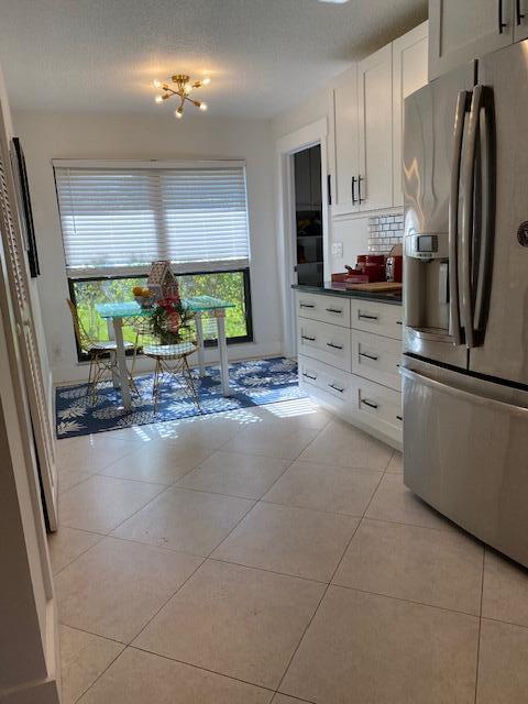 kitchen with light tile patterned floors, white cabinetry, decorative backsplash, dark countertops, and stainless steel fridge