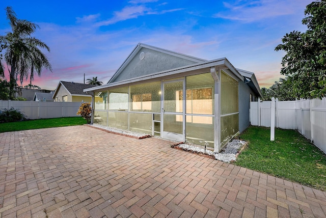 back house at dusk featuring a patio, a sunroom, and a lawn