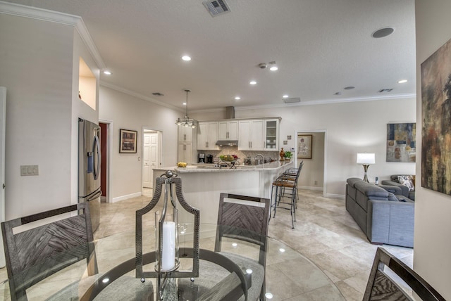 kitchen featuring a breakfast bar area, visible vents, glass insert cabinets, stainless steel refrigerator with ice dispenser, and white cabinetry